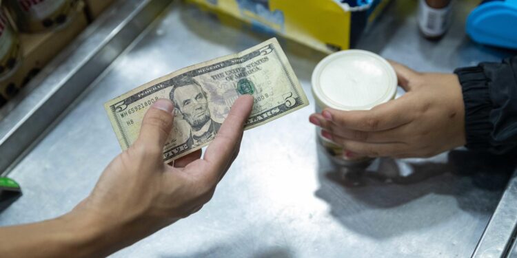 AME458. CARACAS (VENEZUELA), 09/07/2024.- Un hombre paga en una tienda con un billete de cinco dolares estadounidenses, el 8 de julio de 2024, en Caracas (Venezuela). La inflación en Venezuela, que en junio cayó hasta el 1 %, se ha desacelerado a raíz de una política para estabilizar el precio del dólar -divisa usada en el país para cotizar bienes y servicios-, para lo que también se han "sacrificado" salarios y créditos bancarios, advierten expertos. EFE/ Ronald Peña