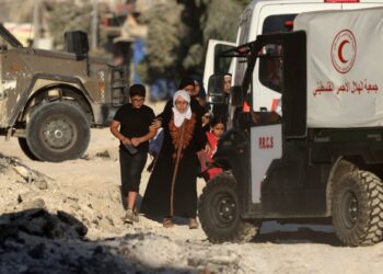 Members of a Palestinian family fleeing an Israeli raid in the Nur Shams camp near the city of Tulkarem in the Israeli-occupied West Bank, walk past Red Crescent ambulances stationed outside the camp on August 28, 2024. - At least 10 Palestinians were killed in Israeli raids and strikes in several towns in the north of the occupied West Bank, a spokesman for the Red Crescent said on August 28. (Photo by JAAFAR ASHTIYEH / AFP)