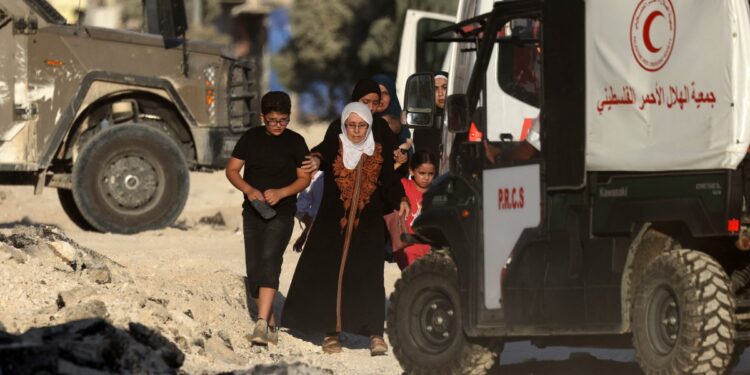 Members of a Palestinian family fleeing an Israeli raid in the Nur Shams camp near the city of Tulkarem in the Israeli-occupied West Bank, walk past Red Crescent ambulances stationed outside the camp on August 28, 2024. - At least 10 Palestinians were killed in Israeli raids and strikes in several towns in the north of the occupied West Bank, a spokesman for the Red Crescent said on August 28. (Photo by JAAFAR ASHTIYEH / AFP)