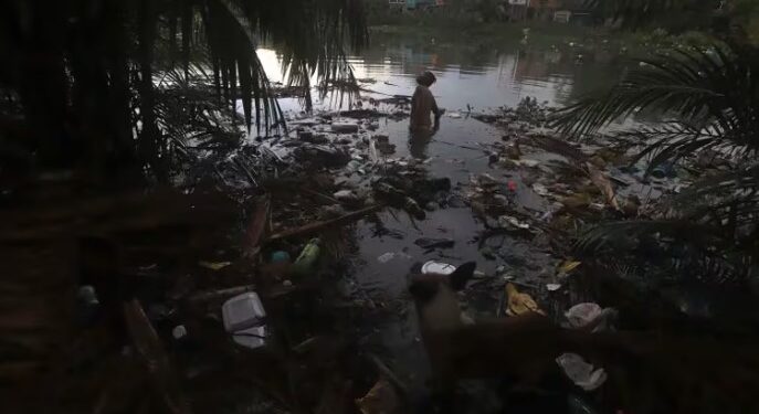 Un residente vadea entre la basura que ensucia las aguas del canal de Sao Joaquim, en el vecindario de Barreiro, en Belem, Brasil (AP FotoPaulo Santos).