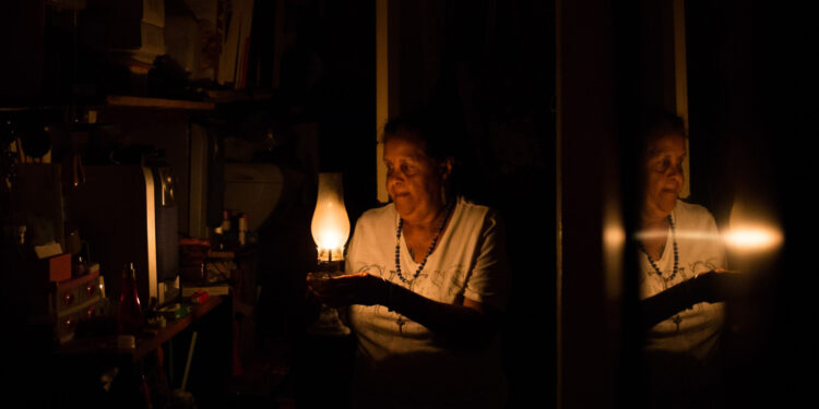 Venezuelan Elvia Helena Lozano is reflected in a mirror as she uses a kerosene lamp during a power outage at her home in Caracas on March 9, 2019. - Sunday is the third day Venezuelans remain without communications, electricity or water, in an unprecedented power outage that already left 15 patients dead and threatens with extending indefinitely, increasing distress for the severe political and economic crisis hitting the oil-rich South American nation.  ¿Podrá salvar la comida en la nevera? ¿Cuánto durará el agua que recogió en tobos? ¿Acabará el "toque de queda" de la delincuencia en la oscuridad? Son preguntas que atormentan a Yadira mientras espera que el suministro de electricidad sea normalizado en Venezuela. (Photo by Cristian HERNANDEZ / AFP)