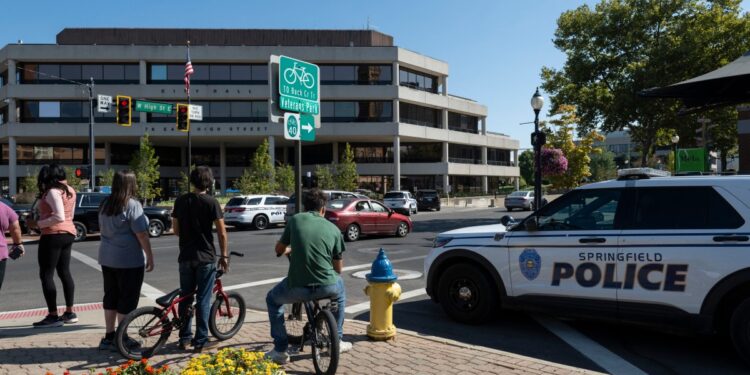 People watch as Springfield Police Department officers investigate the Springfield City Hall after bomb threats were made against buildings earlier in the day in Springfield, Ohio on September 12, 2024. - A government building and school were evacuated after an alleged bomb threat Thursday in Springfield, Ohio, local media reported, rattling the small city at the heart of an anti-migrant conspiracy theory amplified by Donald Trump. Springfield has been thrust into the spotlight in recent days after an unfounded story of Haitian migrants eating pets went viral on social media, with the Republican ex-president and current White House candidate pushing the narrative despite it being debunked. (Photo by ROBERTO SCHMIDT / AFP)