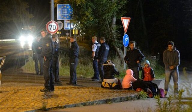 La policía federal alemana aguarda junto a varios refugiados que esperan en la frontera entre Freilassing, Alemania, y Salzburgo, Austria, el lunes 14 de septiembre de 2015. Alemania reintrodujo los controles temporales de frontera el domingo para reducir el ritmo de llegada de los miles de refugiados que cruzan su frontera, enviando un claro mensaje a sus socios europeos de que necesita más ayuda para lidiar con la crisis. (AP Foto/Kerstin Joensson)