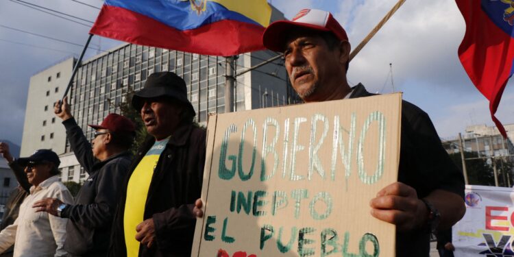 A man holds a sign against the government as he takes part in a march to commemorate the historic workers massacre of 1922 in Quito on November 15, 2024. On November 15, 1922, the government of Ecuador called on the military to suppress the Guayaquil general strike. (Photo by Galo Paguay / AFP)