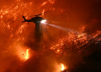 A fire fighting helicopter drops water as the Palisades fire grows near the Mandeville Canyon neighborhood and Encino, California, on January 11, 2025. The Palisades Fire, the largest of the Los Angeles fires, spread toward previously untouched neighborhoods January 11, forcing new evacuations and dimming hopes that the disaster was coming under control. Across the city, at least 11 people have died as multiple fires have ripped through residential areas since January 7, razing thousands of homes in destruction that US President Joe Biden likened to a "war scene." (Photo by Patrick T. Fallon / AFP)